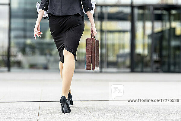 Businesswoman wearing high heels walking with briefcase on footpath
