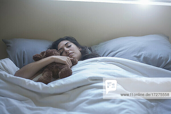 Young woman holding toy while sleeping on bed at home