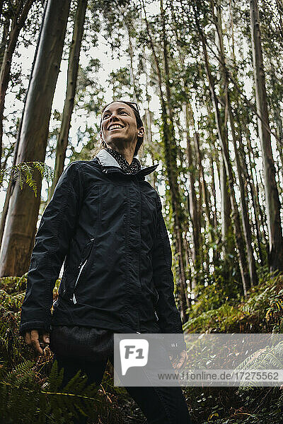 Smiling woman looking away while standing in forest during rainy season
