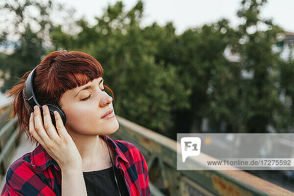 Redhead woman with eyes closed listening music through headphones