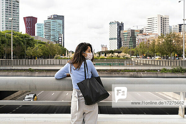 Rückansicht einer Frau mit Handtasche an einem Geländer in der Stadt während COVID-19