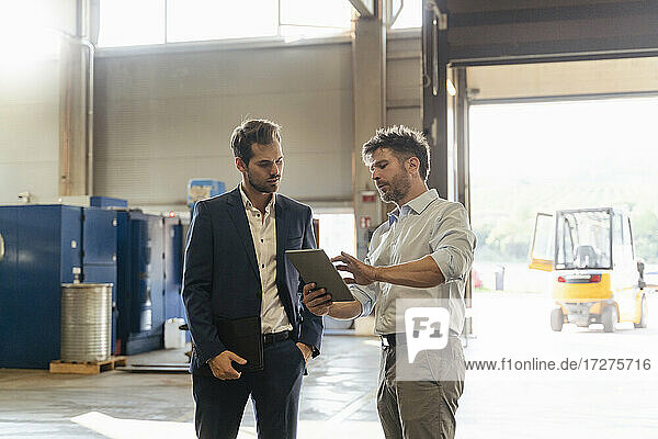 Mature man using digital tablet while discussing with businessman at factory