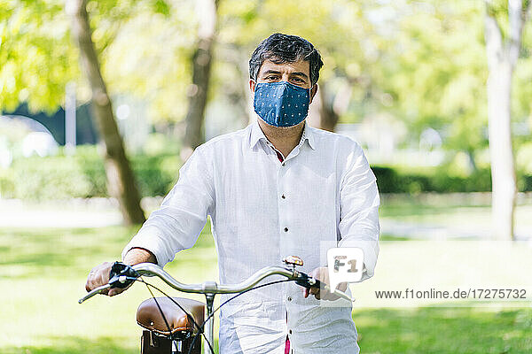 Älterer Mann mit Gesichtsschutzmaske und Fahrrad in einem öffentlichen Park während COVID-19