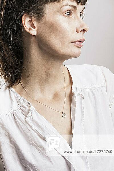 Close-up of woman wearing necklace looking away in studio