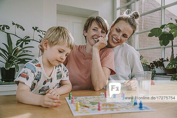 Mütter schauen zu  während ihr Sohn zu Hause ein Brettspiel spielt