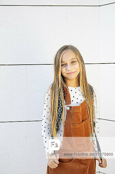 Blond girl smiling while standing against wall on sunny day