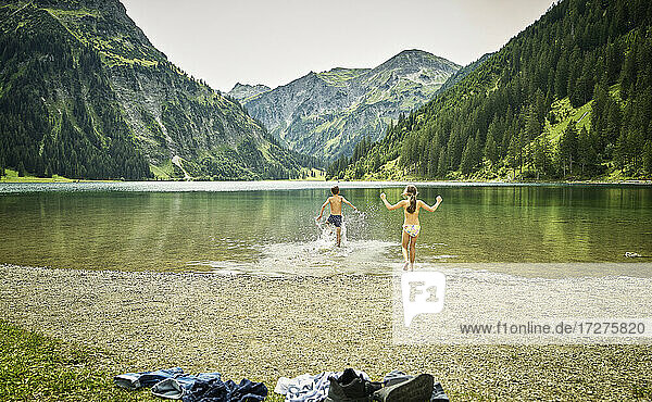 Siblings running at lakeshore while enjoying vacation