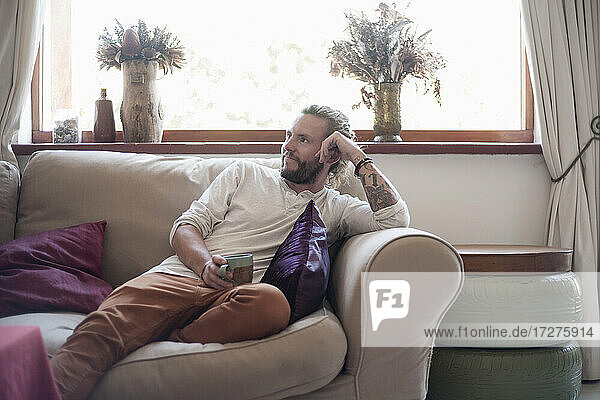 Männlicher Hipster trinkt Kaffee und entspannt sich auf dem Sofa zu Hause