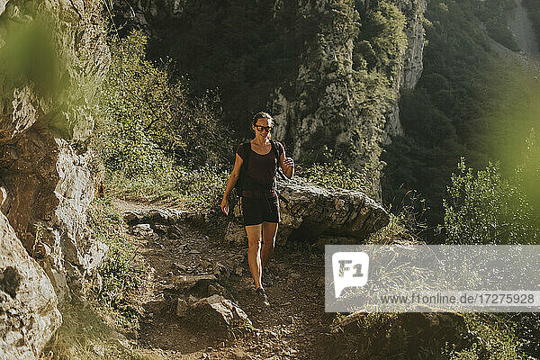Female trekker hiking downhill on trail during sunny day