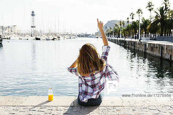 Young woman with arms raised looking at sea on sunny day
