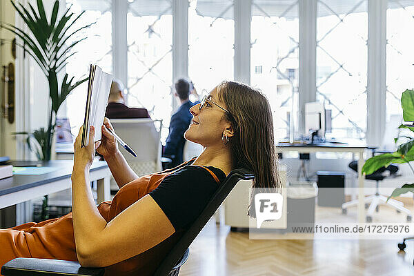 Lächelnde Geschäftsfrau beim Tagebuchlesen im Büro