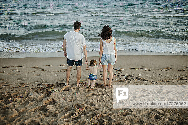 Husband and wife with son looking at view while standing on beach during sunset
