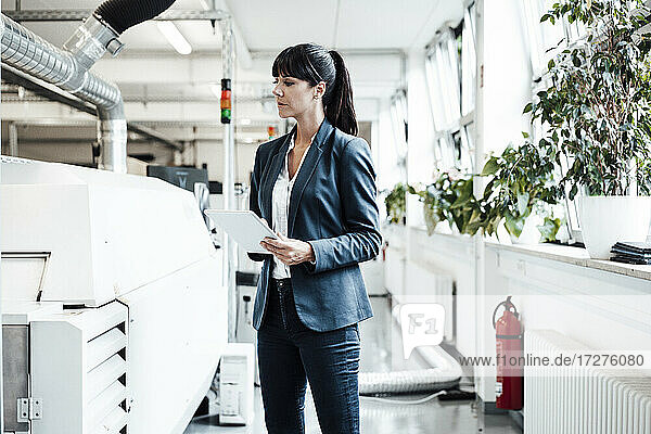 Geschäftsfrau  die Maschinen betrachtet und ein digitales Tablet in der Hand hält