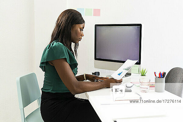 Geschäftsfrau analysiert Millimeterpapier  während sie am Schreibtisch im Büro sitzt