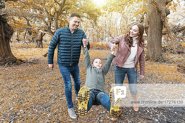 Parents playing with their kid in park during autumn