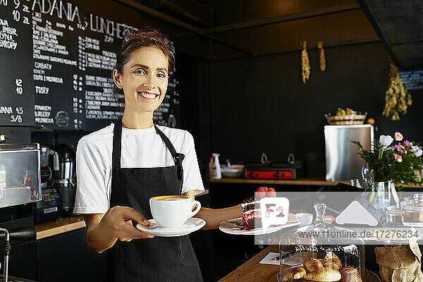 Porträt einer lächelnden Kellnerin  die Kaffee und Gebäck in einem Café serviert