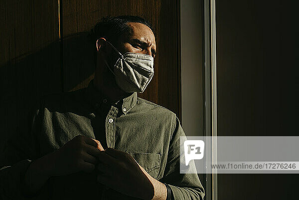 Mann mit Gesichtsschutzmaske beim Wegschauen zu Hause