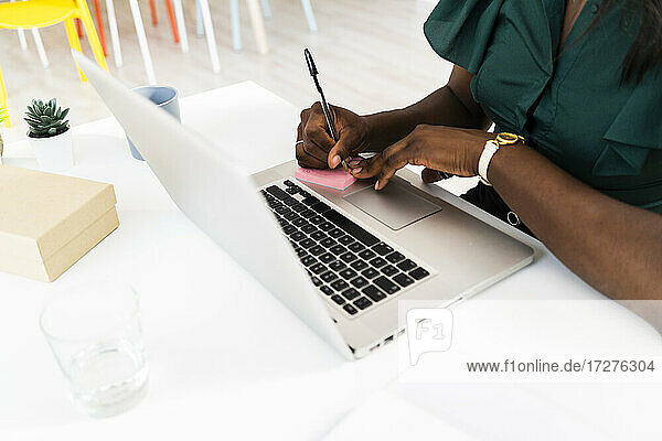 Geschäftsfrau schreibt auf Haftnotiz  während sie am Laptop im Büro arbeitet
