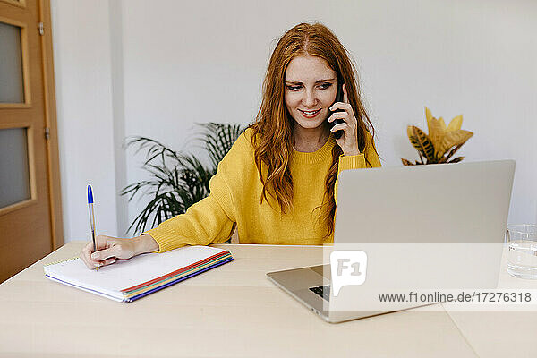 Junge Frau  die beim Schreiben zu Hause mit ihrem Smartphone telefoniert