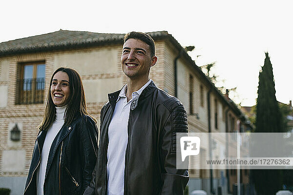 Lächelnder Freund und Freundin schauen weg  während sie auf der Straße in der Stadt spazieren gehen