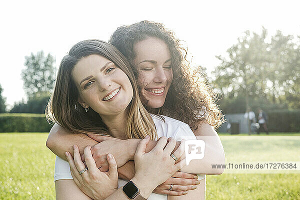 Schöne Frau wird von einer lächelnden jungen Freundin im Park umarmt