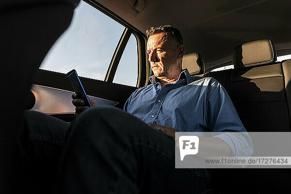 Reifer männlicher Unternehmer  der im Auto sitzend ein Smartphone benutzt