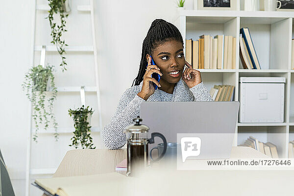 Nachdenkliche Frau  die mit ihrem Smartphone spricht  während sie zu Hause am Laptop lernt