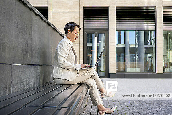 Frau benutzt Laptop  während sie auf einer Bank vor einem Gebäude sitzt