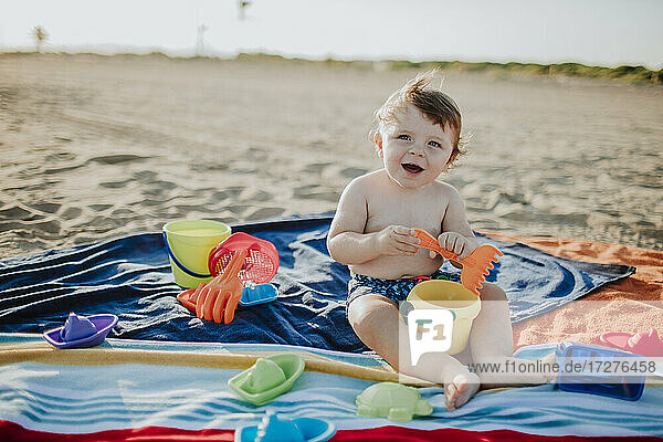 Glückliches männliches Kleinkind,  das beim Spielen am Strand wegschaut