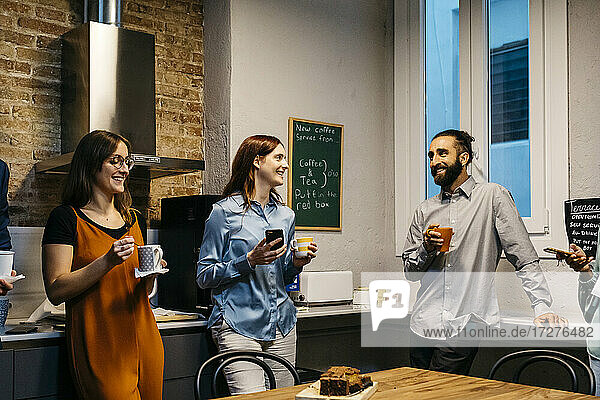Lächelnde männliche und weibliche Unternehmer diskutieren bei einem Kaffee in der Küche am Arbeitsplatz