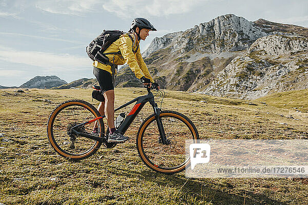 Mid adult woman with backpack riding bicycle on mountain at Somiedo Natural Park  Spain