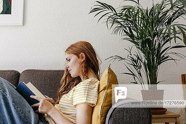 Junge Frau liest ein Buch  während sie zu Hause auf dem Sofa liegt