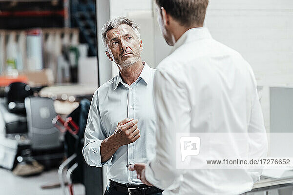 Mature businessman discussing with colleague while standing in factory