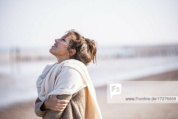 Lächelnde Frau mit verschränkten Armen und Blick auf den Strand an einem sonnigen Tag