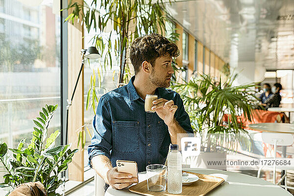 Businessman looking away while drinking coffee at table in cafe
