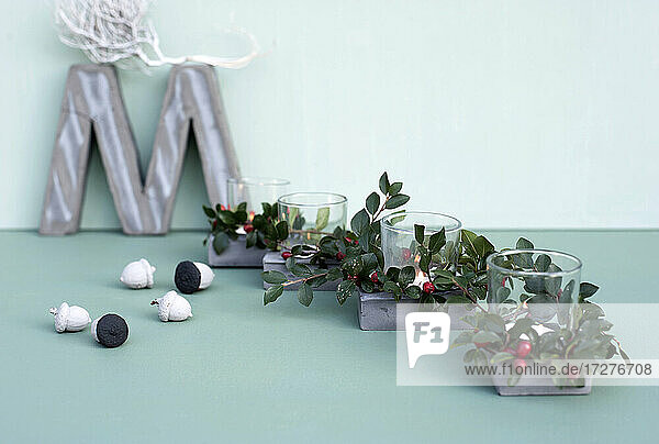 Concrete letter M  painted acorns and candles inside glasses decorated with twigs of cotoneaster