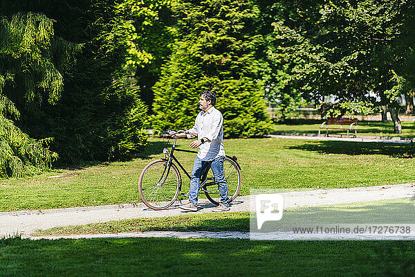 Mature man looking away while walking with bicycle in public park