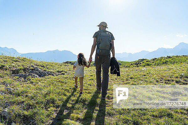 Father and daughter walking on grass during summer