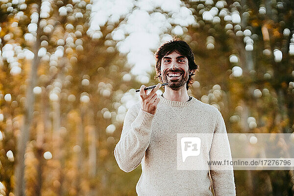 Smiling man talking on mobile phone while standing at forest
