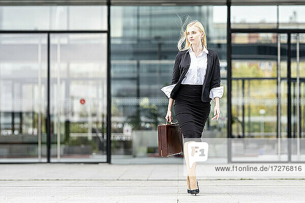 Geschäftsfrau schaut weg  während sie mit einer Aktentasche gegen ein Gebäude läuft