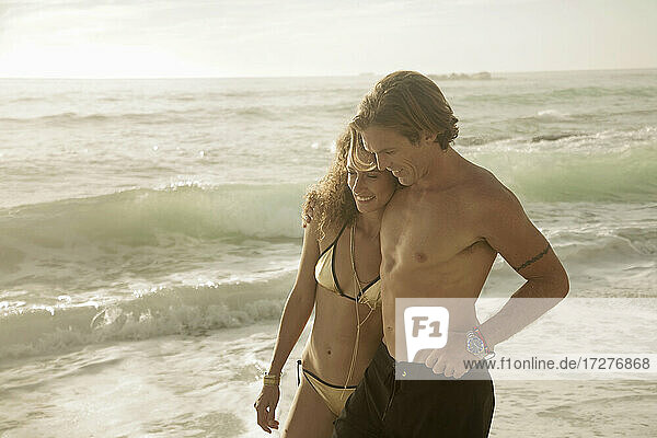 Lächelndes Paar  das sich umarmt  während es am Strand an einem sonnigen Tag im Wasser steht