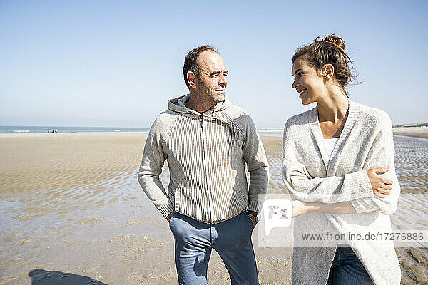 Lächelnde Tochter und Vater im Gespräch beim Spaziergang am Strand