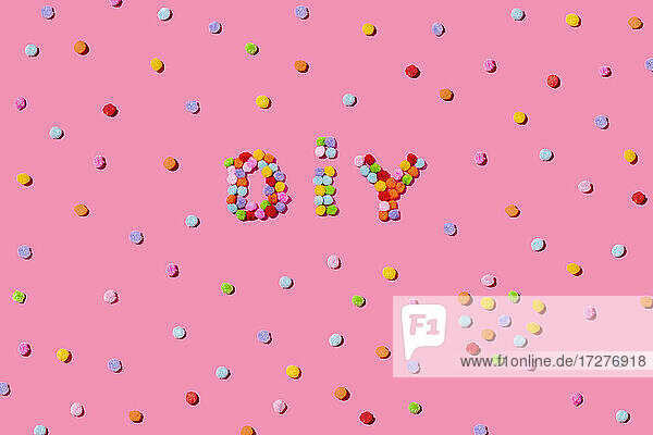 DIY Text arrangiert mit bunten Pom Poms auf rosa Hintergrund