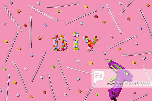 DIY Text arrangiert mit bunten flauschigen Pom Poms und Klebepistole auf rosa Hintergrund im Studio