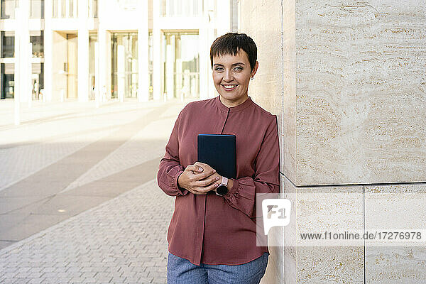 Businesswoman holding digital tablet while leaning on wall