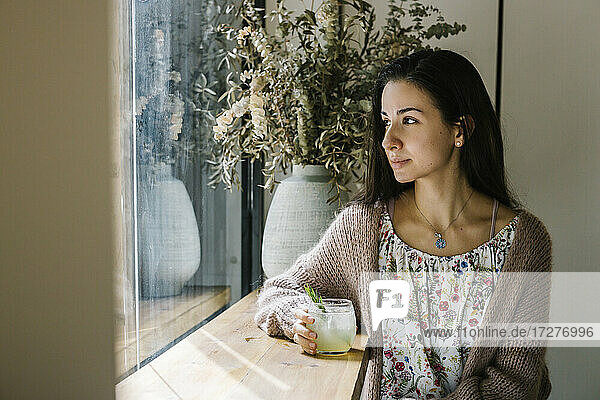 Junge Frau mit Limonadenglas schaut durch das Fenster  während sie in einem Café sitzt