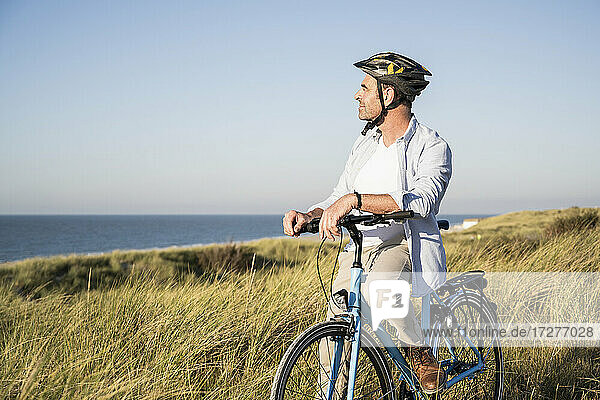 Man looking at view while sitting on bicycle by grassy field against clear sky