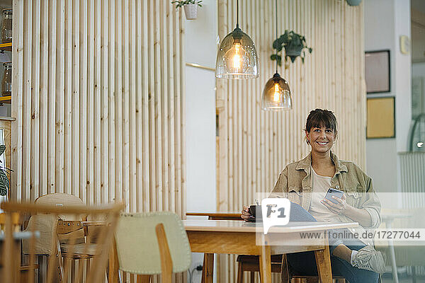 Lächelnde Geschäftsfrau  die ein Smartphone benutzt  während sie in einem Café sitzt