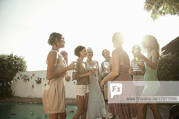 Glückliche Freunde  die den Sommer genießen  während sie am Pool gegen den Himmel Alkohol trinken