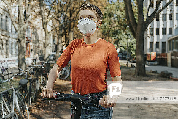 Frau mit schützendem Gesicht beim Fahren eines Elektrorollers auf der Straße an einem sonnigen Tag